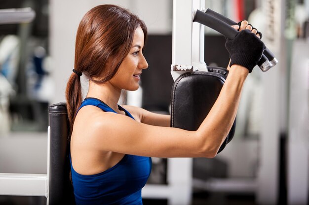 Linda mujer joven con un traje deportivo y guantes haciendo ejercicio en un simulador en el gimnasio