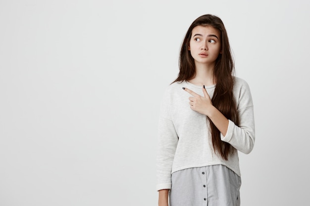 Linda mujer morena alegre joven apuntando con el dedo índice, mostrando algo interesante y emocionante