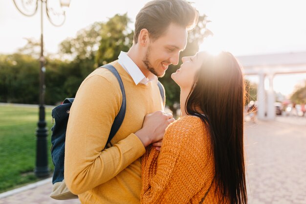 Linda mujer de pelo largo en suéter naranja tejido mirando a los ojos de su novio con amor en el soleado día de otoño