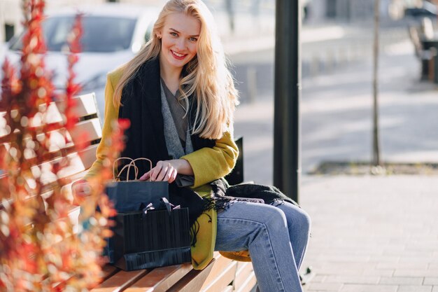 Linda mujer rubia atractiva feliz con paquetes en la calle en un clima cálido y soleado