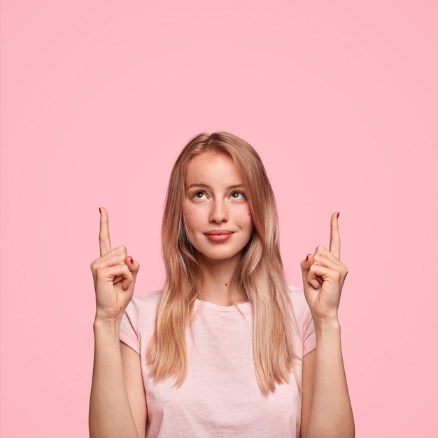 Linda mujer rubia con pelo largo, indica con dos dedos hacia arriba