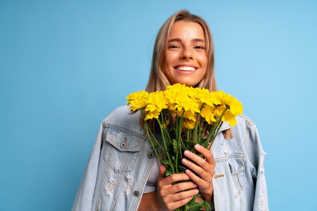 Linda mujer rubia posando en fondo azul con gran ramo de flores amarillas, tiempo de primavera.