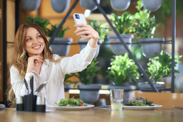 Linda mujer sentada en la cafetería y haciendo selfie