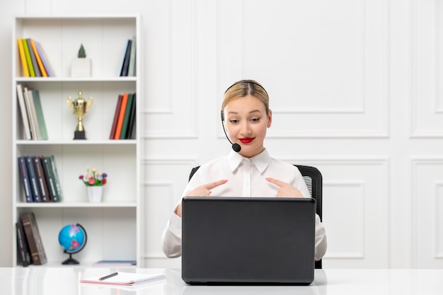 Linda mujer de servicio al cliente con camisa blanca con auriculares y computadora apuntándose a sí misma