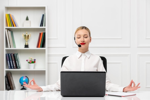 Linda mujer de servicio al cliente en camisa blanca con auriculares y computadora mostrando gesto zen