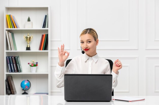 Linda mujer de servicio al cliente con camisa blanca con auriculares y computadora que muestra un gesto correcto