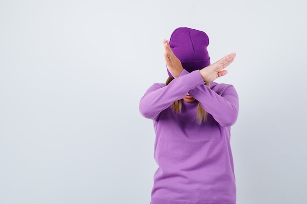 Linda mujer en suéter, gorro que muestra un gesto de rechazo y una mirada decidida, vista frontal.