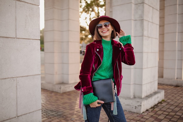 Foto gratuita linda mujer en traje de moda de estilo otoñal caminando en la calle vistiendo chaqueta de terciopelo púrpura, gafas de sol y sombrero