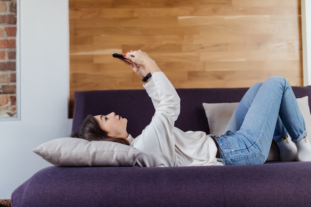 Linda mujer usando un teléfono inteligente acostado en una cama en su casa