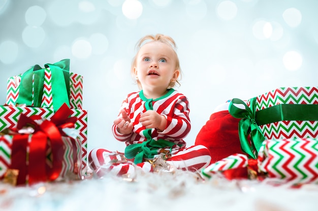 Linda niña de 1 año cerca de sombrero de santa posando sobre Navidad con decoración. Sentado en el suelo con bola de Navidad