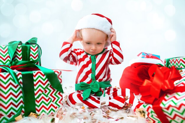 Linda niña de 1 año vistiendo gorro de Papá Noel posando sobre adornos navideños