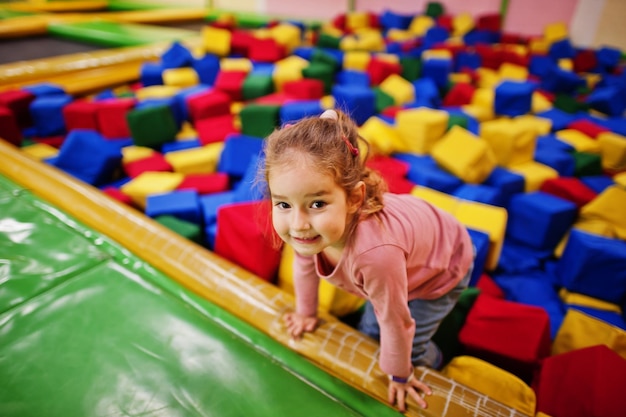 Foto gratuita linda niña acostada en la piscina con cubos de espuma de colores en el centro de juegos interior