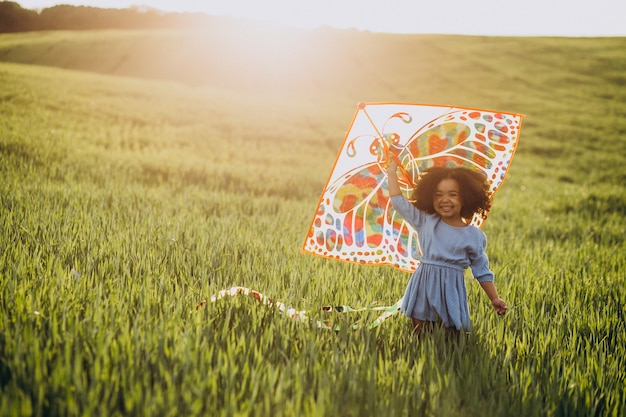 Linda niña africana en el campo en la puesta de sol jugando con cometa