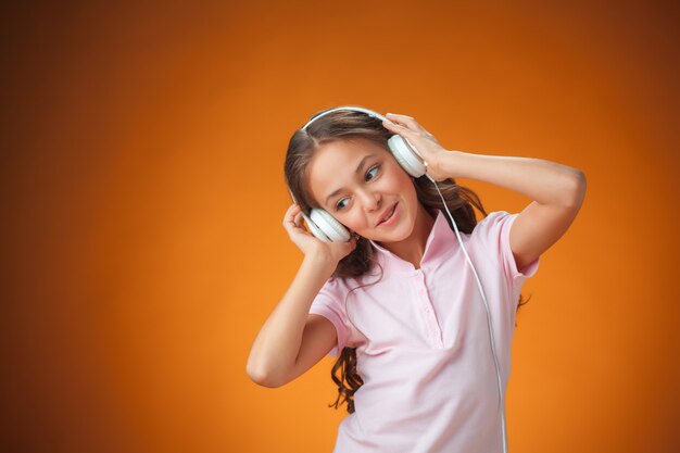 La linda niña alegre con auriculares en pared naranja