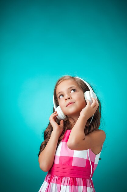 La linda niña alegre con auriculares en pared naranja