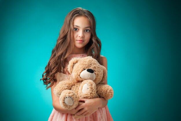 La linda niña alegre con osito de peluche en la pared azul