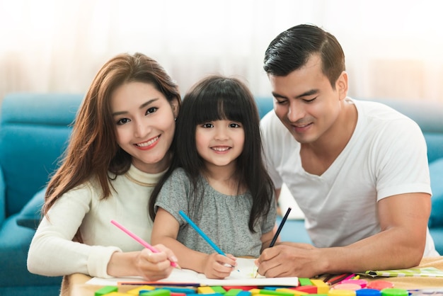 Linda niña de cabello negro, hija, tarea y risa junto con los padres en el concepto de casa de la sala de estar