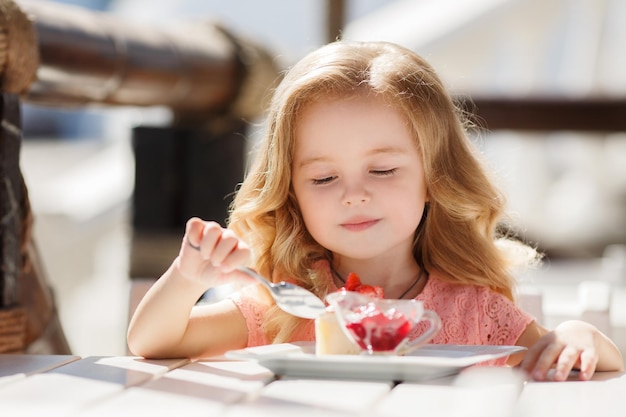 linda niña comiendo postre en la terraza del café