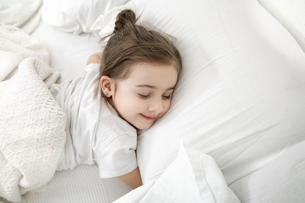 Una linda niña está durmiendo en una cama blanca.