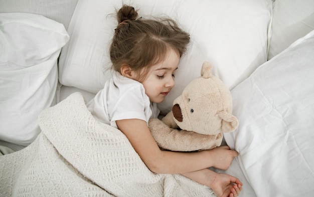 Una linda niña está durmiendo en una cama con un osito de peluche. Concepto de sueño y desarrollo infantil. La vista desde arriba.