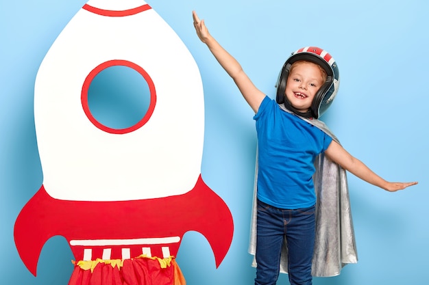 Linda niña feliz juega astronauta, lleva casco y capa voladores