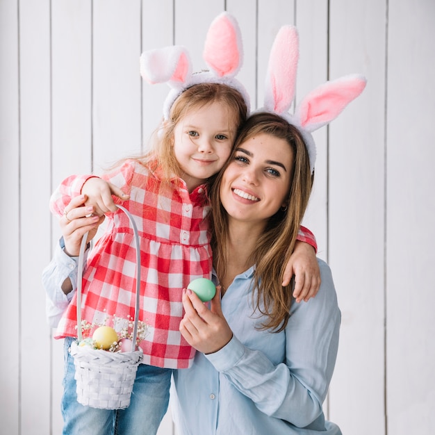 Linda niña y madre de pie con canasta de huevos de Pascua