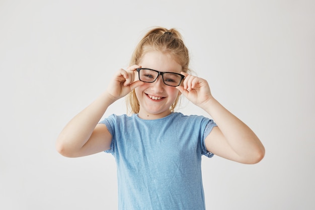 Linda niña con ojos azules y cabello claro sonrisas juega con mamá tomando sus lentes y probándose. Felices momentos familiares.