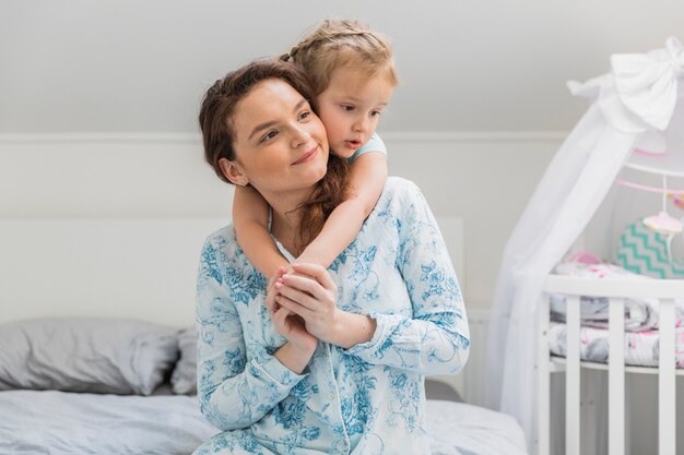 Linda niña pequeña abrazando a su madre en la cama