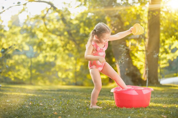 La linda niña rubia jugando con agua salpica en el campo en verano