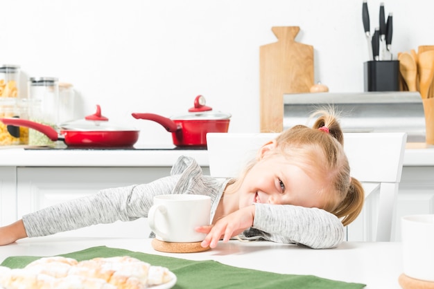 Linda niña sonriente con blanco taza de té y desayuno