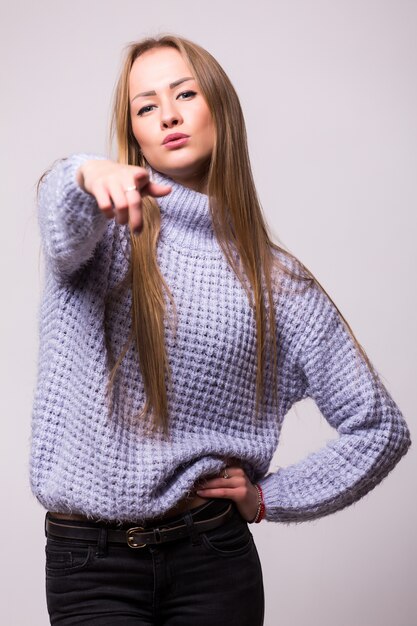 Linda niña sonriente joven apuntando a usted aislado en la pared blanca