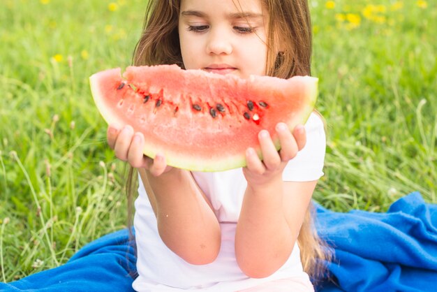 Linda niña sosteniendo una rodaja de sandía roja en el parque