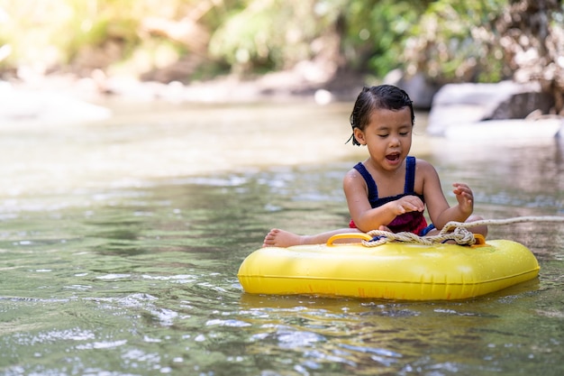 Linda niña del sudeste asiático en una balsa flotante amarilla en un río