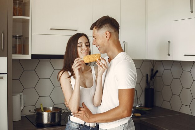 Linda pareja en una cocina. Señora con una camiseta blanca. Par en casa comer maíz hervido.