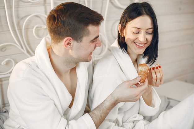 Linda pareja en el dormitorio con albornoces desayunando.