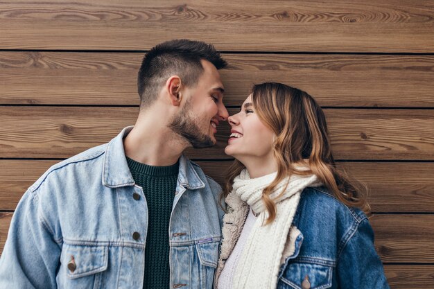 Linda pareja europea posando juntos en un día frío. Foto interior de chica rubia en chaqueta vaquera besando a su novio.