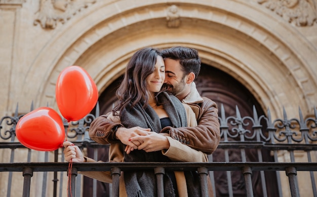 Foto gratuita linda pareja con globos abrazándose cerca de la cerca