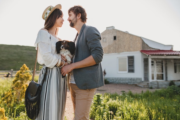 Linda pareja hipster bastante elegante enamorada caminando con perro en el campo, moda boho de estilo veraniego, romántico