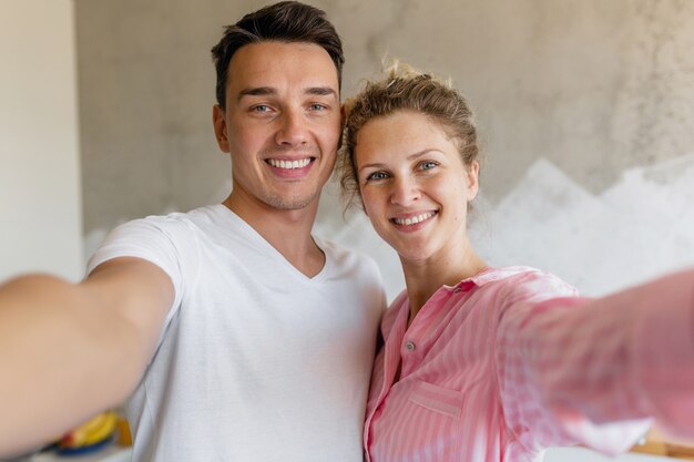 Linda pareja joven divirtiéndose en el dormitorio por la mañana, hombre y mujer haciendo foto selfie en pijama