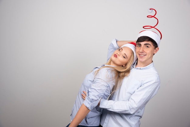 Linda pareja joven de pie en sombrero de Navidad y posando