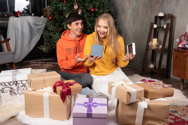 Linda pareja joven sentada y abriendo regalos cerca del árbol de navidad