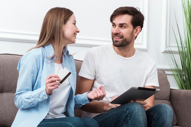 Linda pareja mirándose y sosteniendo dispositivos digitales para compras en línea