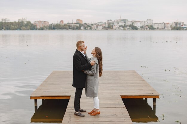 Linda pareja en un parque. Dama con un abrigo gris. Gente en el muelle.