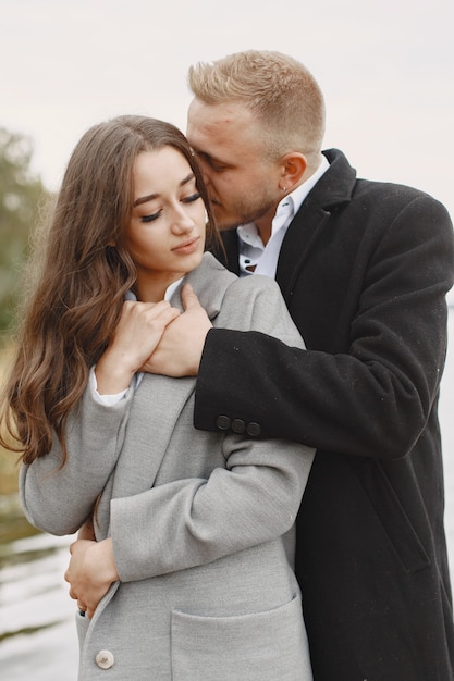 Linda pareja en un parque. Dama con un abrigo gris. Gente en el muelle.