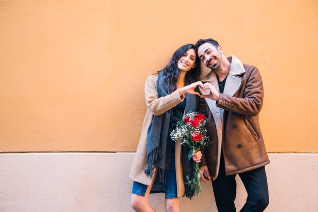 Linda pareja con ramo que muestra gesto de corazón