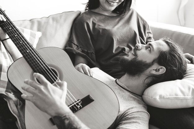 Linda pareja en un sofá novio tocando la guitarra y el concepto de amor