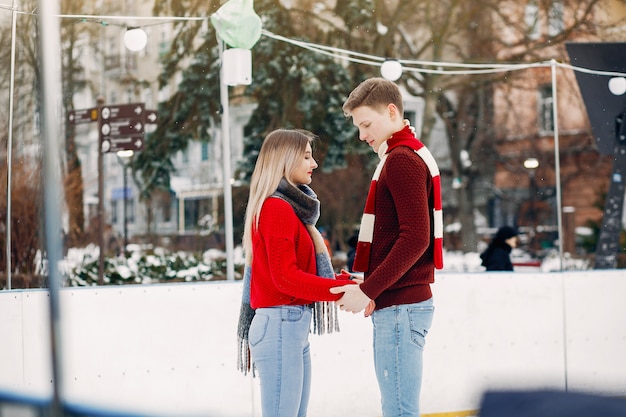 Linda pareja en un suéter rojo divirtiéndose en una arena de hielo