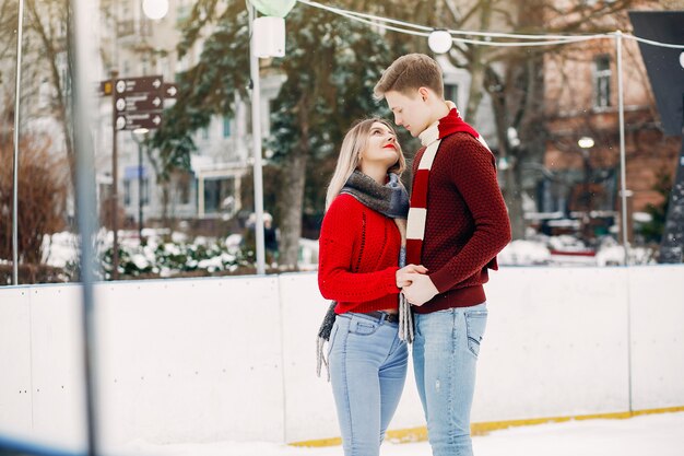 Linda pareja en un suéter rojo divirtiéndose en una arena de hielo