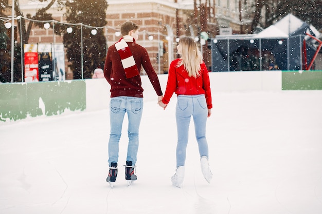 Linda pareja en un suéter rojo divirtiéndose en una arena de hielo