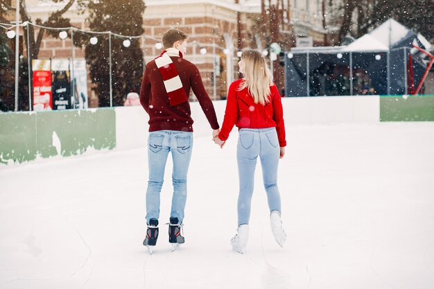 Linda pareja en un suéter rojo divirtiéndose en una arena de hielo